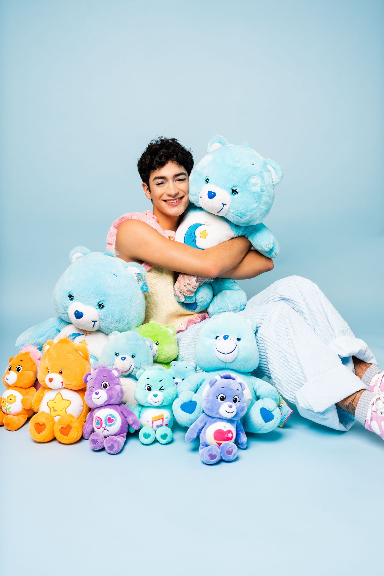 Collection of colorful Care Bears plush toys arranged on light blue background.