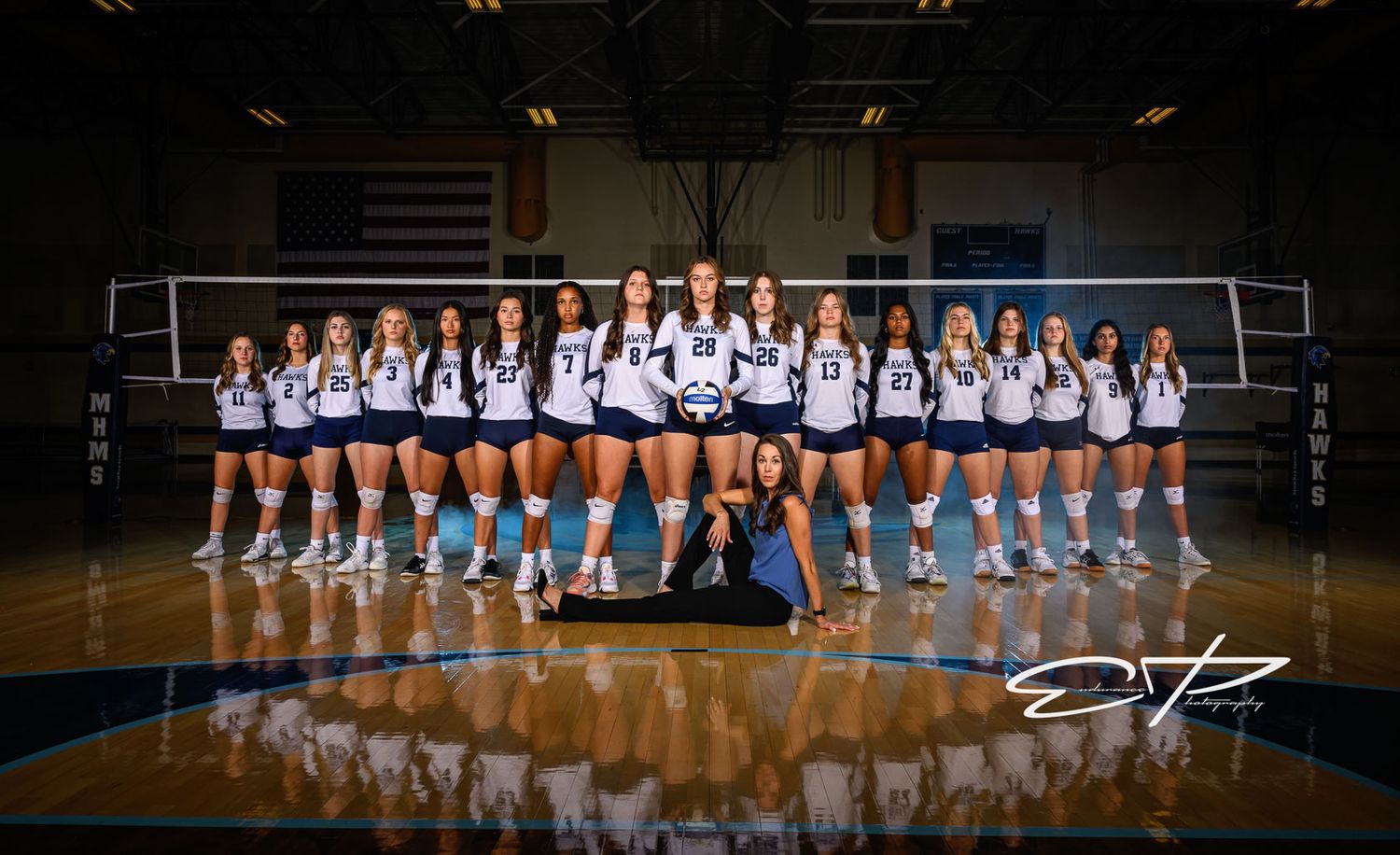 A volleyball team poses for their official team photo on court with American flag in background.