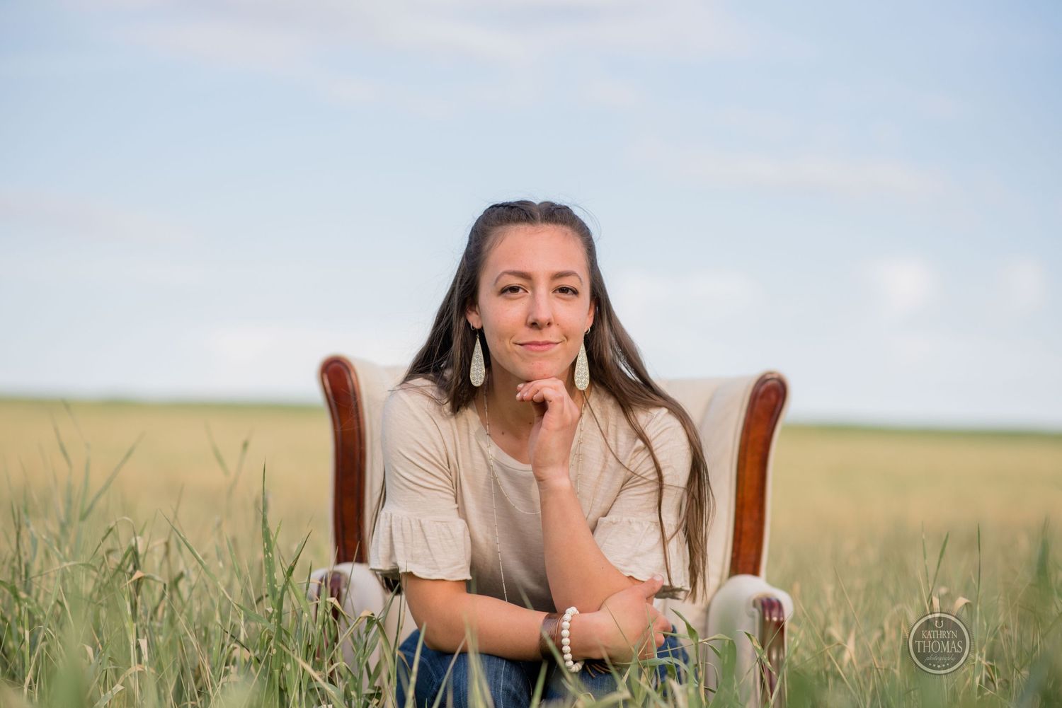 A vintage armchair sits in a meadow as someone poses thoughtfully.
