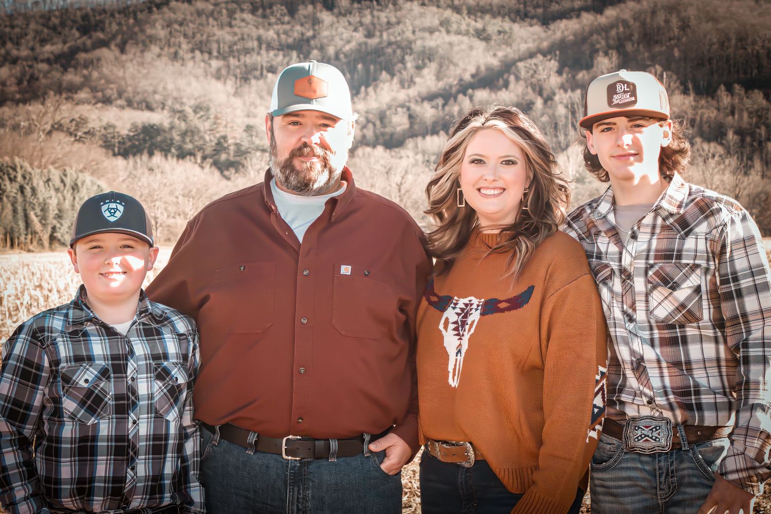 Outdoor family portrait of four people in western wear against mountain backdrop.