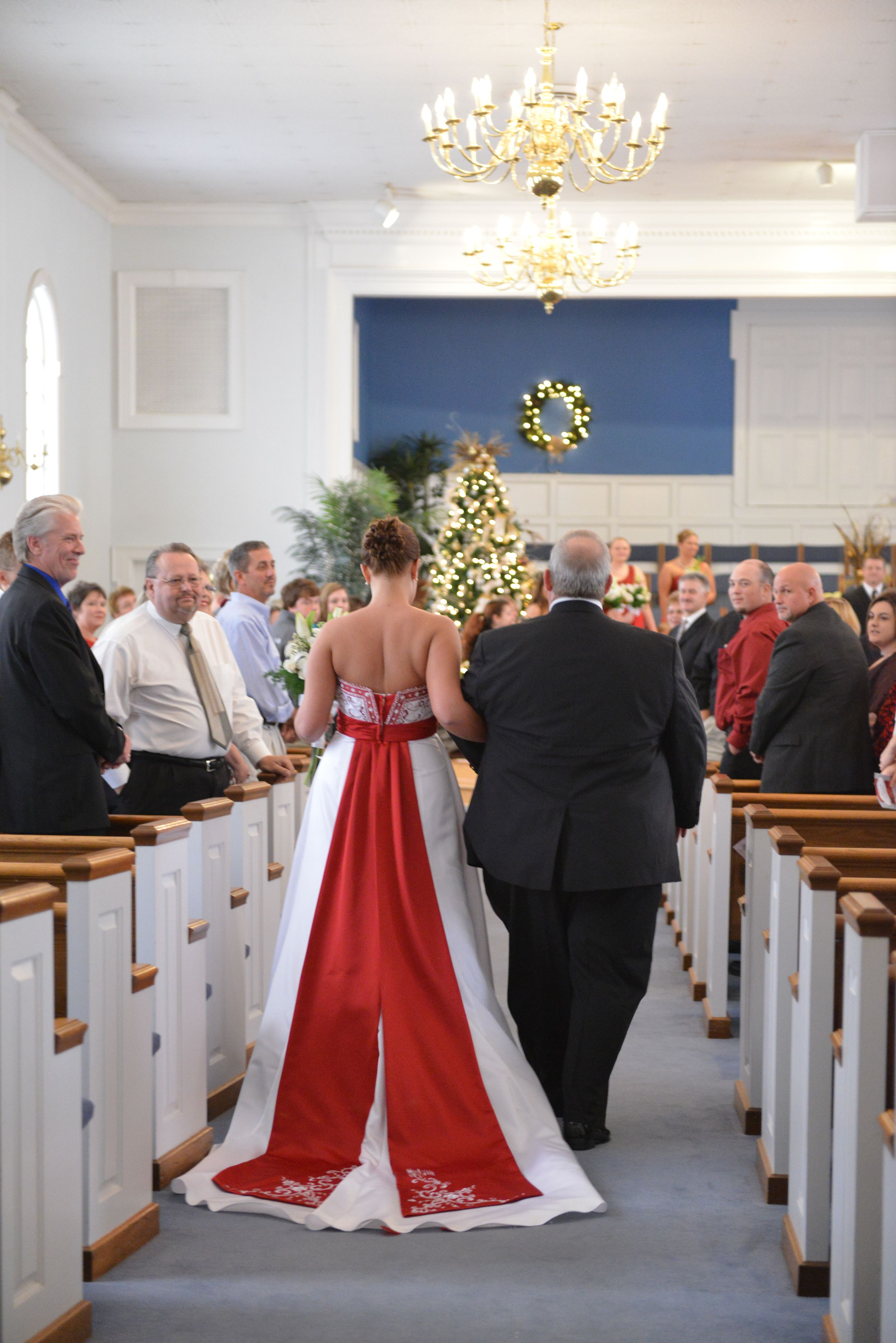 Wedding ceremony in church with red and white decorations and lighted Christmas tree.