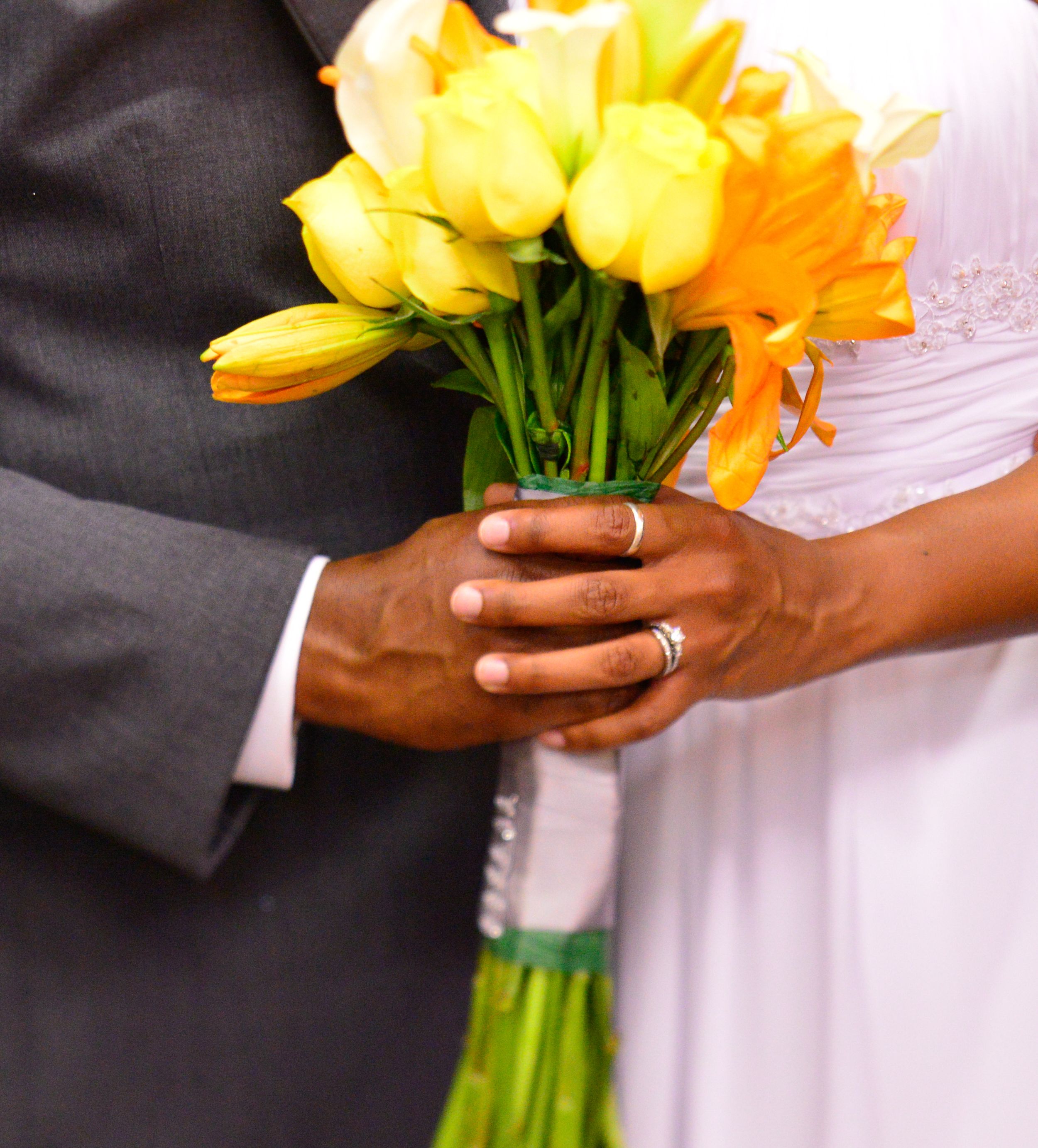 Close-up of hands holding yellow and orange daffodil wedding bouquet.