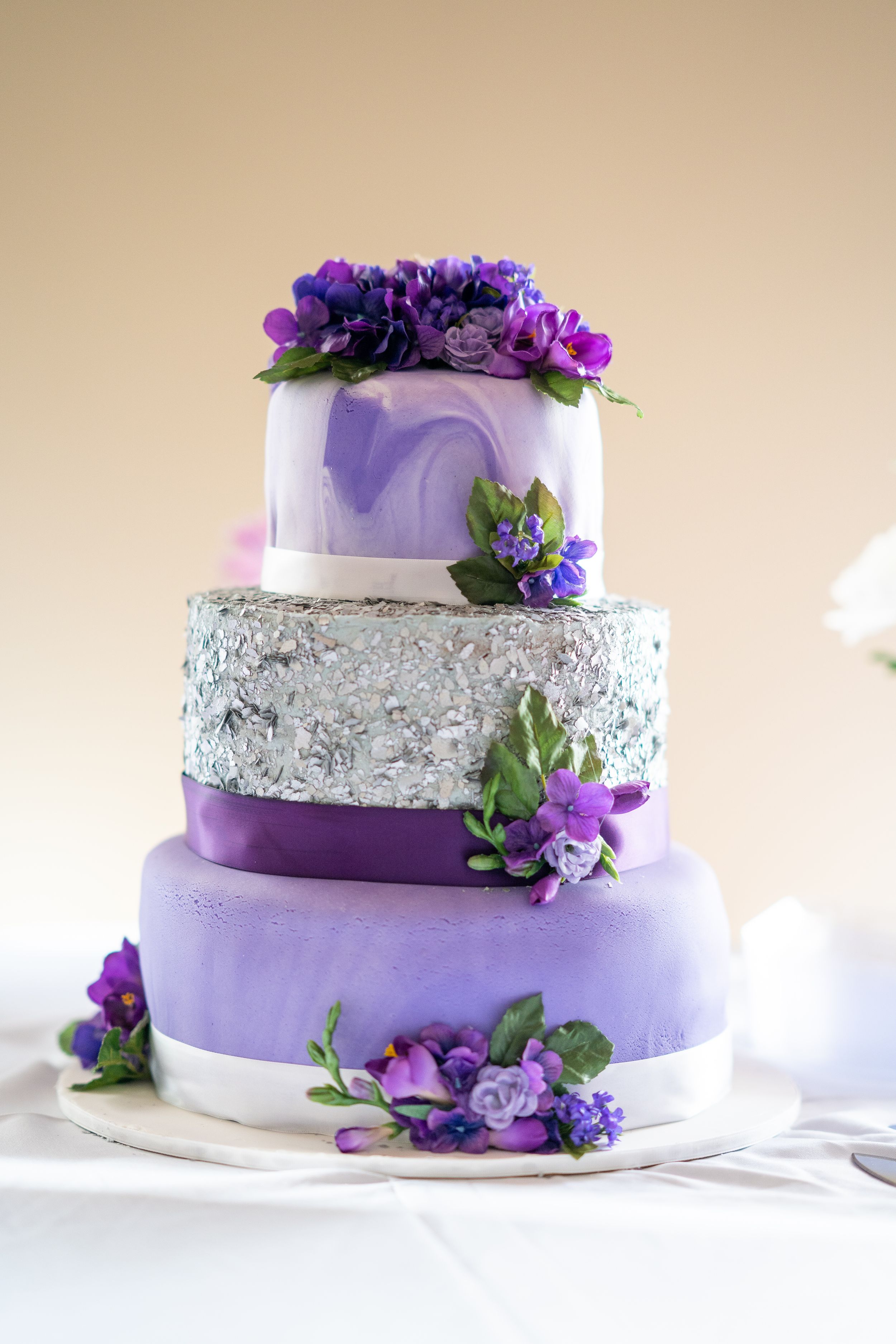 Elegant purple and silver wedding cake adorned with fresh flowers.