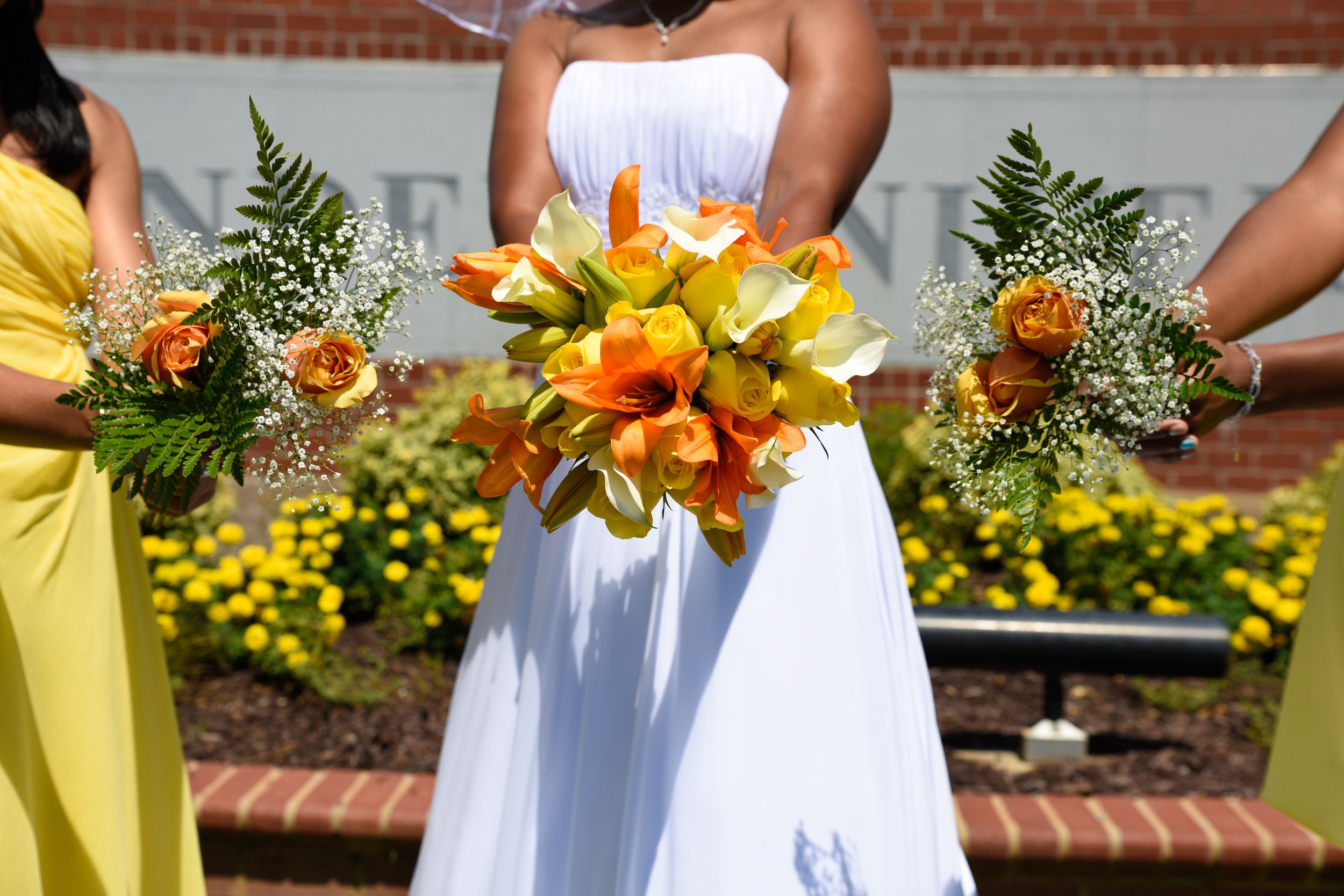 Bridesmaids in white dresses holding vibrant yellow and orange sunflower bouquets.