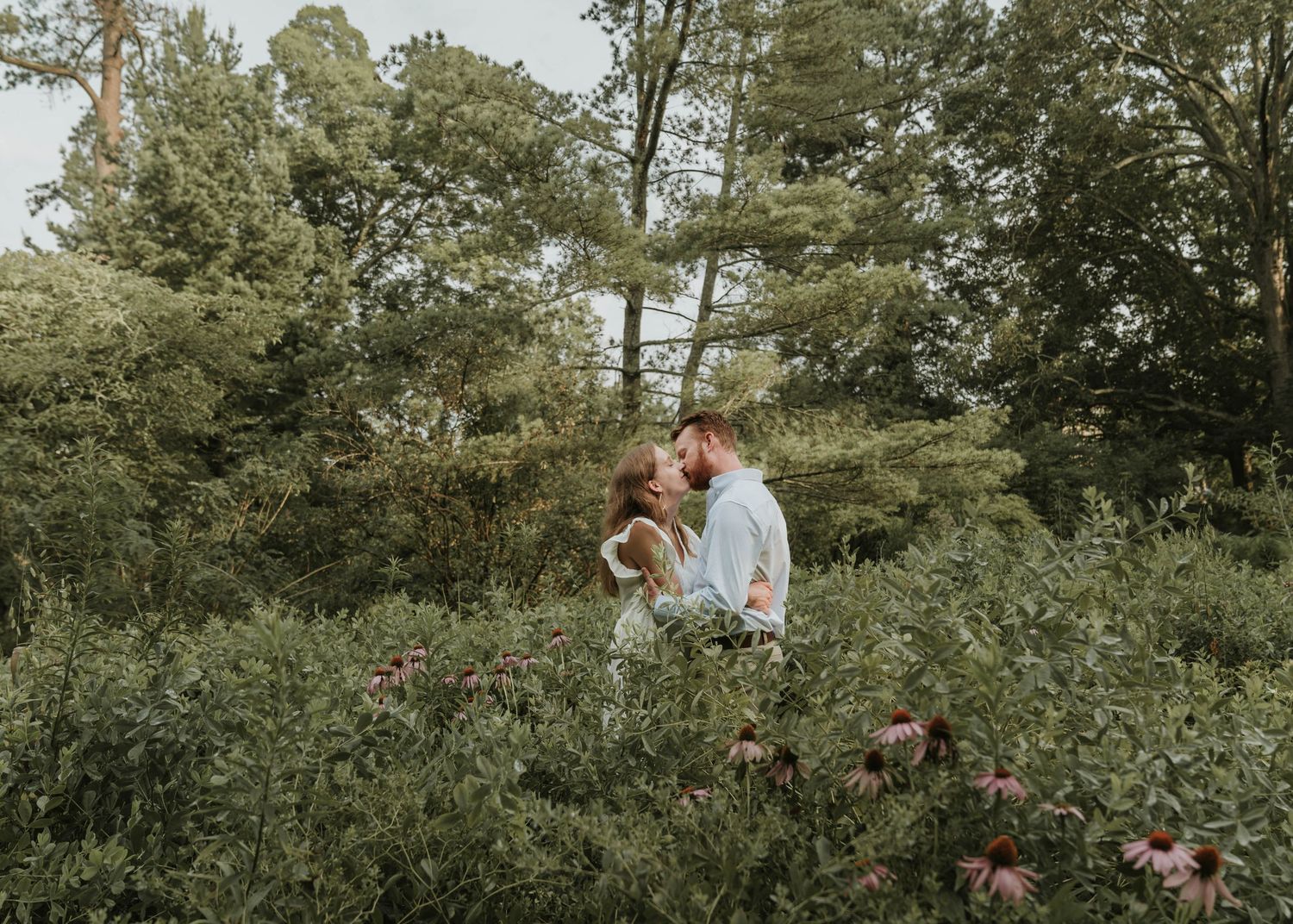 Romantic outdoor portrait of couple sitting among wildflowers and trees.