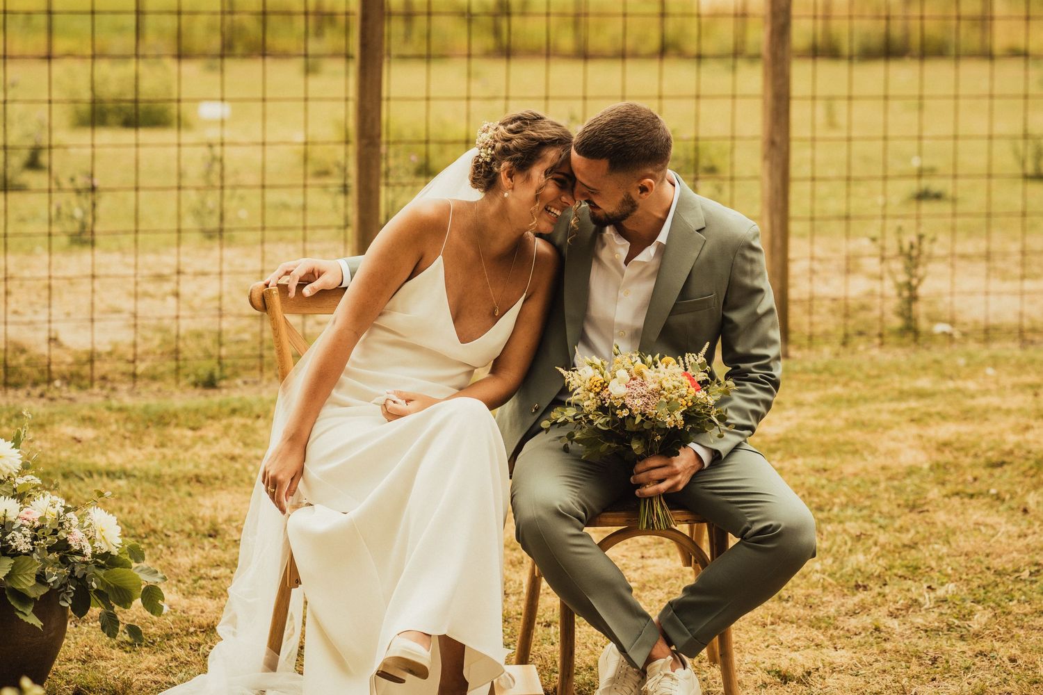 Intimate outdoor wedding ceremony moment with couple on wooden chairs.