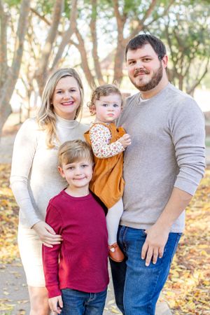 Family of four poses together on wooded path during fall photo session.