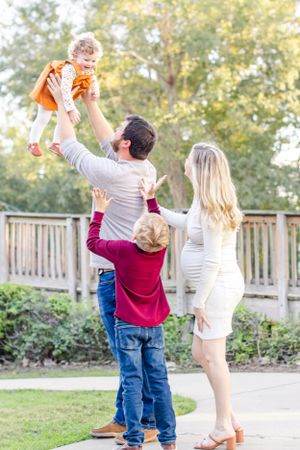 Family plays and lifts children during outdoor photo session on wooden walkway.