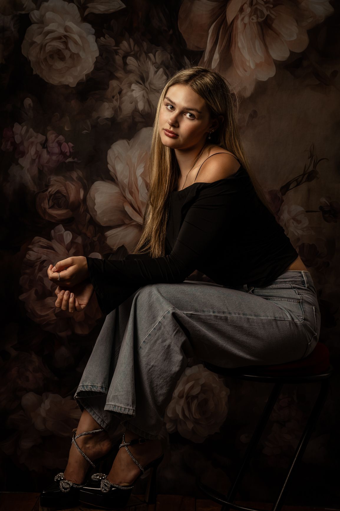 Moody portrait against a dark floral backdrop featuring dramatic lighting and creative pose.