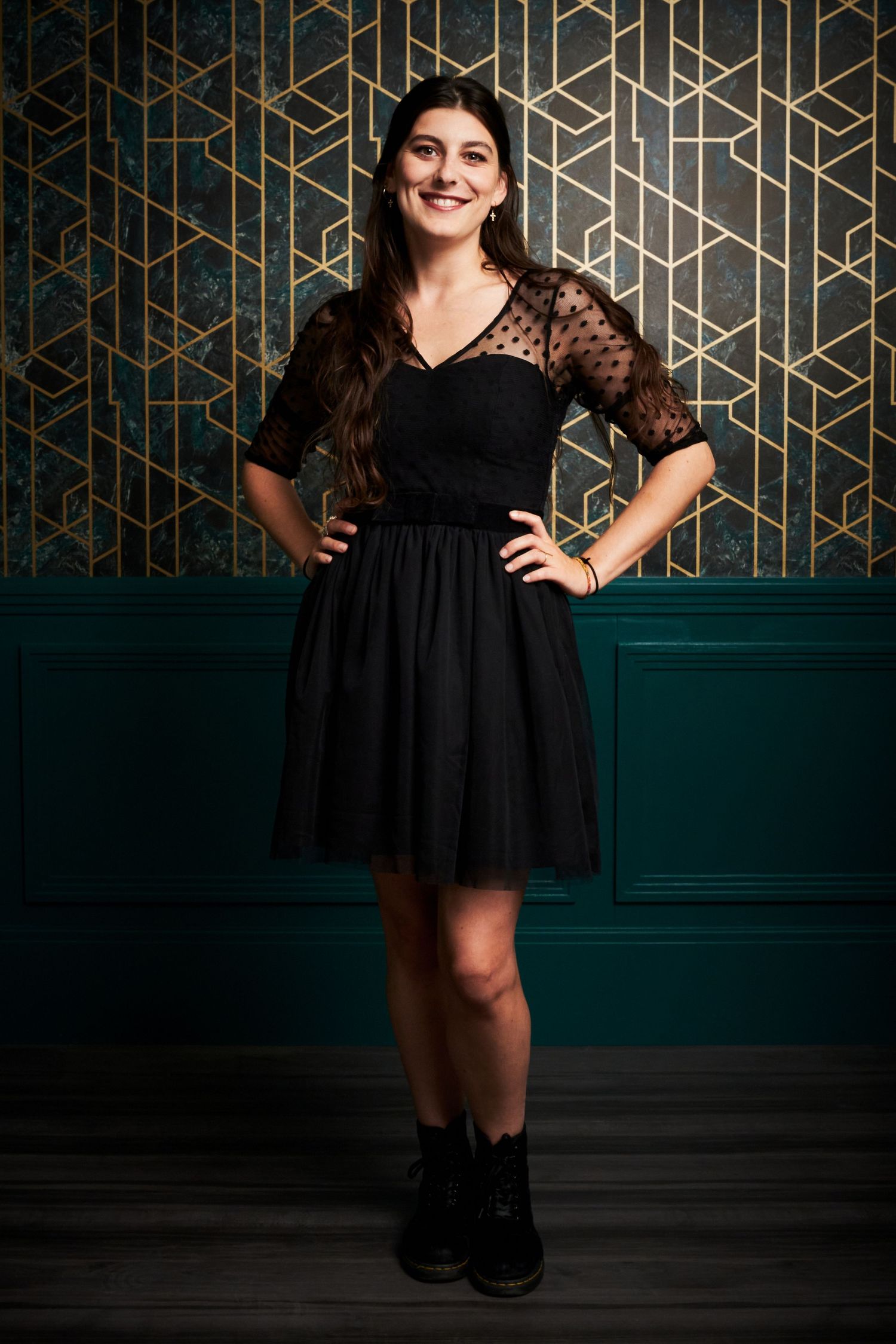 A portrait against an art deco wall featuring a black cocktail dress with lace sleeves.