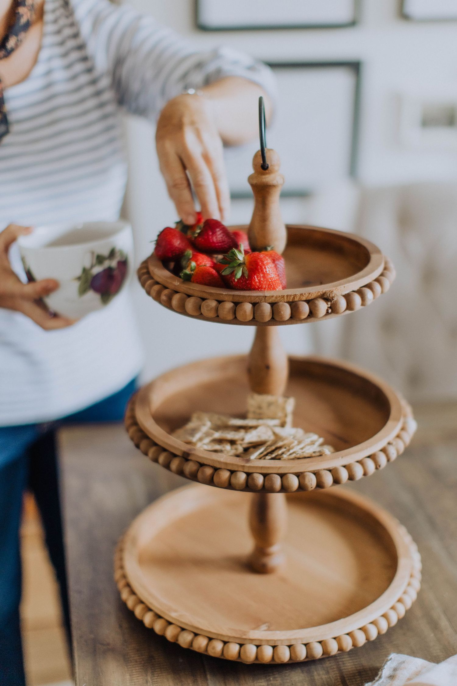 Three-tiered wooden stand with beaded trim being decorated with fresh strawberries.