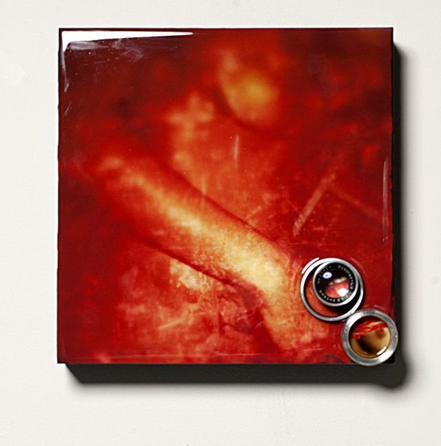 Red textured album cover design with two metallic lens-like circular elements in the bottom right corner.