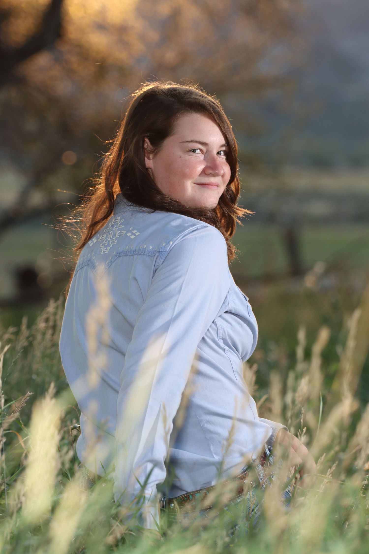 Person in light blue shirt sits in tall grass during golden hour.
