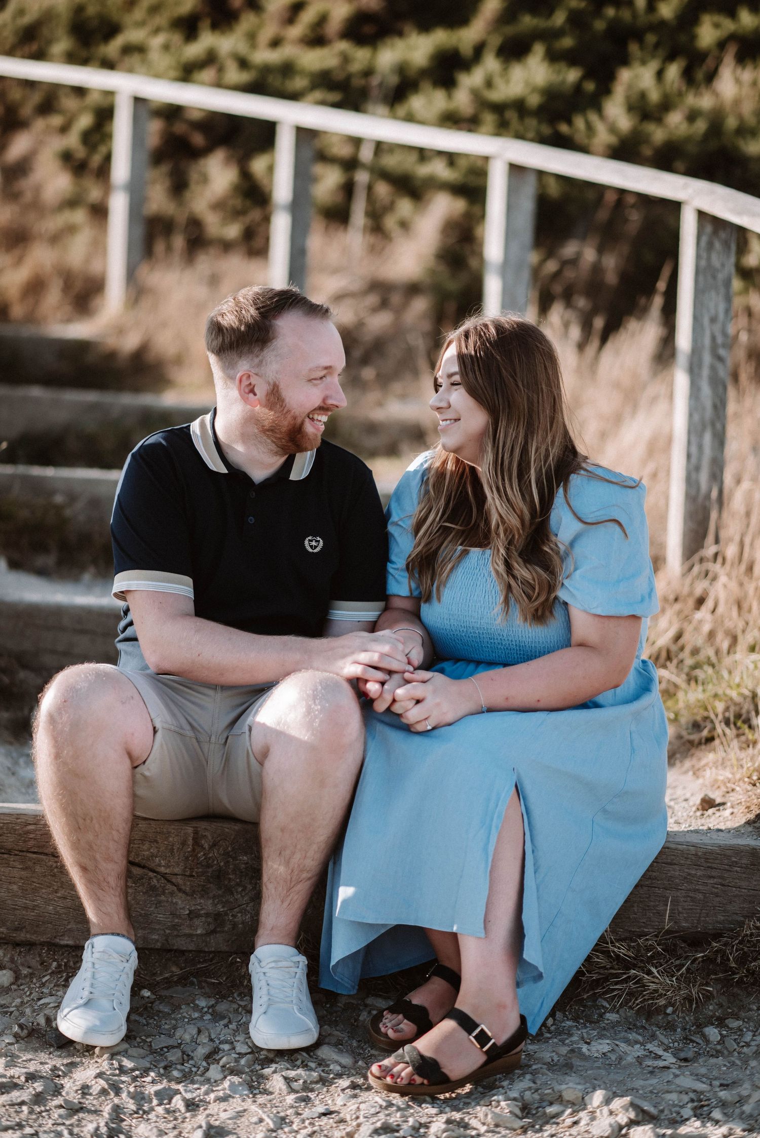 A couple sits together on outdoor steps sharing a tender moment in casual attire.