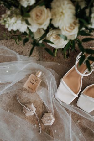 Wedding details with white sandals, perfume bottle and roses on tulle fabric.