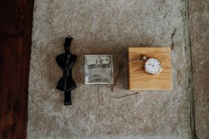 Wedding accessories including bowtie, ring box and pocket watch on wooden surface.