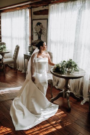 Elegant bridal portrait with flowing white gown in a sunlit room.