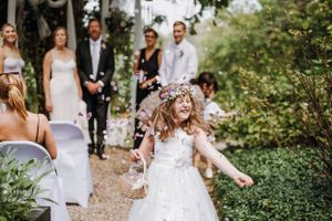 Garden wedding celebration with flower girl dancing down path.