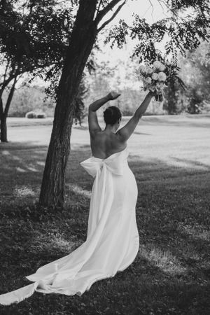 Black and white portrait of bride in backless dress with arms raised in nature.