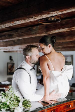 Intimate wedding couple moment captured in rustic indoor setting with wooden beams and floral decor.