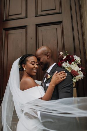 A romantic wedding moment in front of a wooden door with a flowing veil and bouquet.