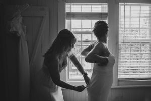 A black and white photo capturing final wedding dress adjustments in front of a window.