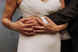 Close-up of hands clasped together showing wedding rings against a light colored dress.