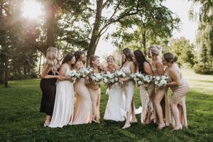 Wedding party bridesmaids laughing together outdoors in light colored dresses holding white flower bouquets.