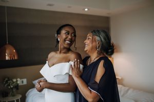 A touching candid moment shared between a bride in white and an older woman in navy during wedding preparations.