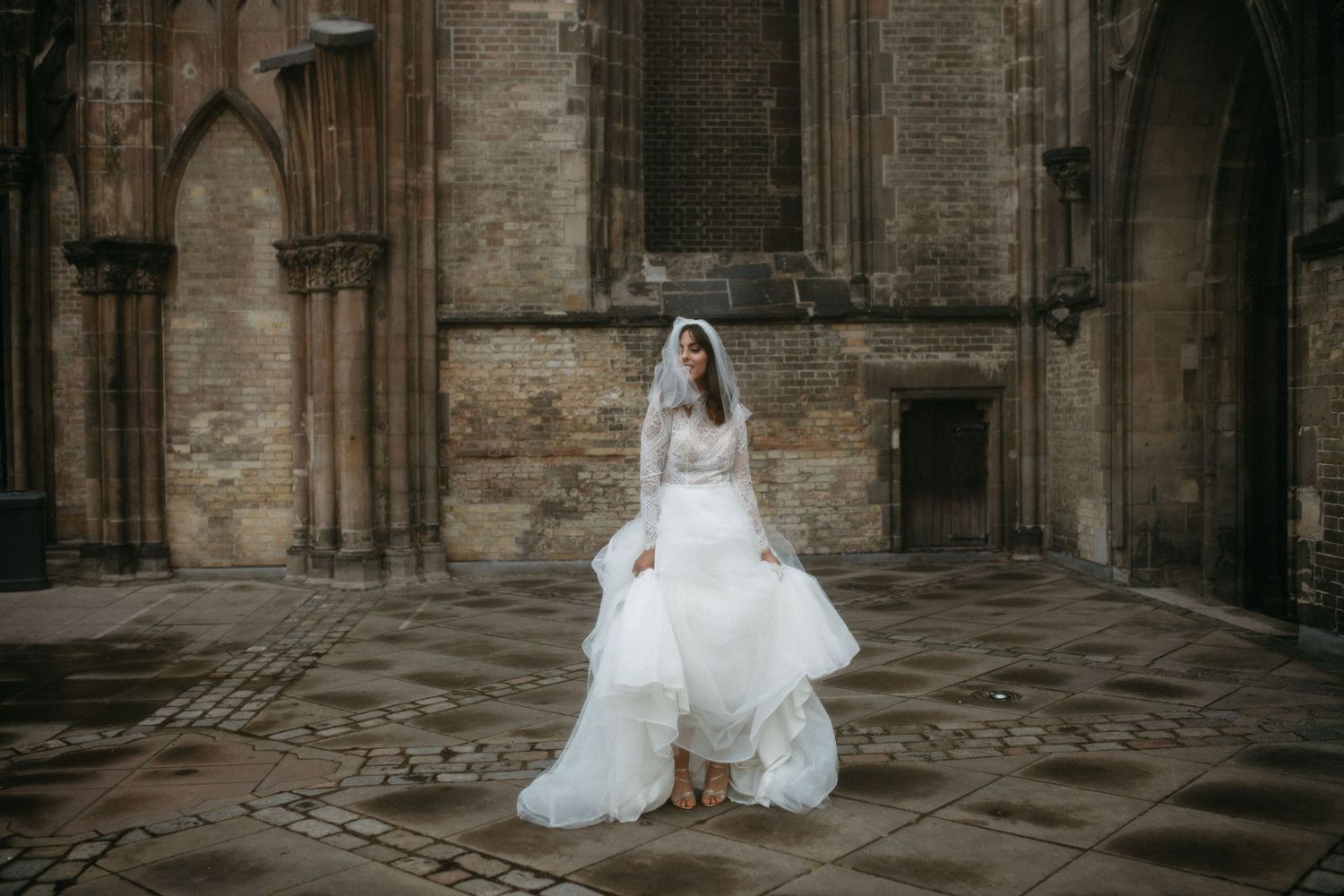 Bride in white lace dress photographed against historic church exterior.