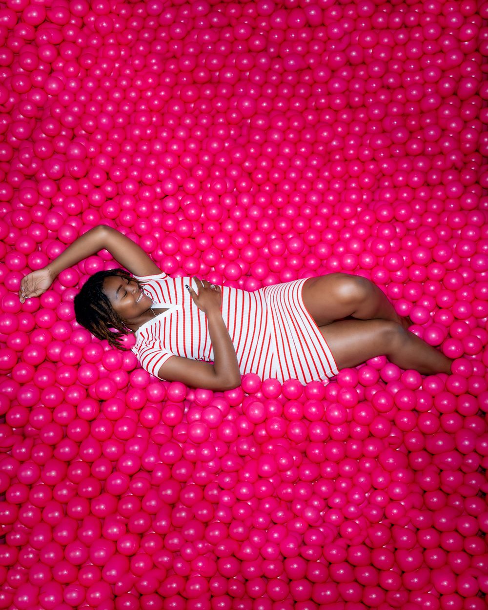 A person in striped dress reclines on bright pink polka dot background.