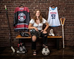 Sports equipment and jerseys displayed on brick wall with athlete posed on bench.