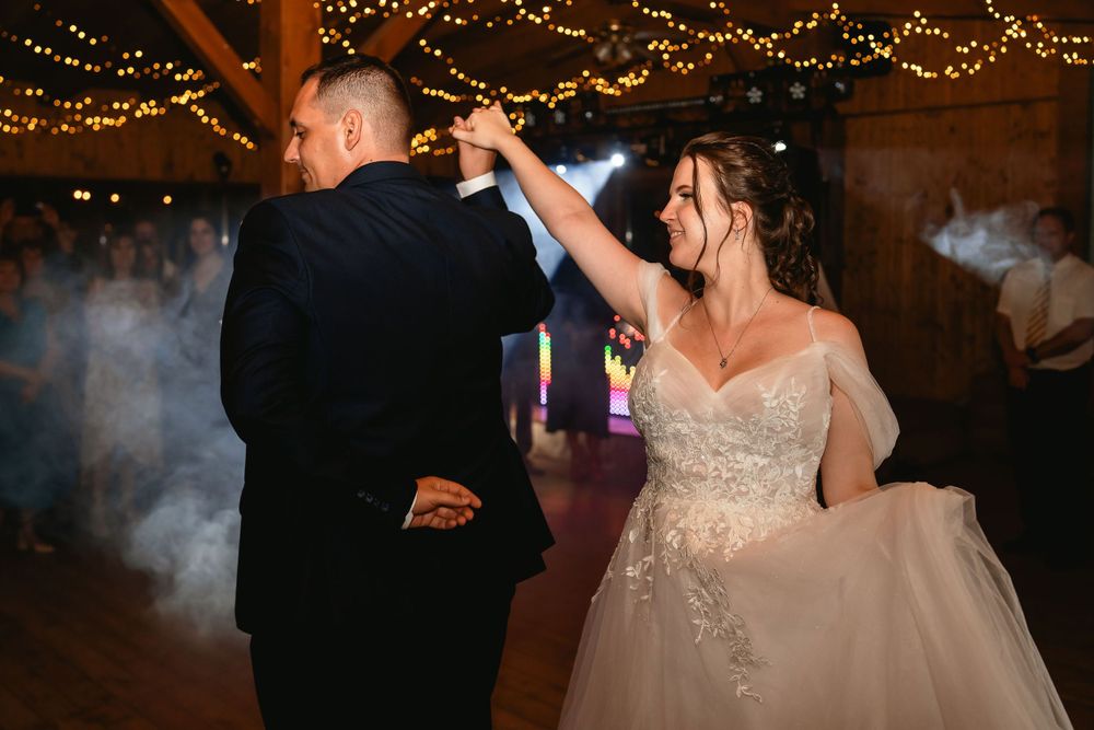 Couple shares a lively dance moment under twinkling lights at their wedding reception.