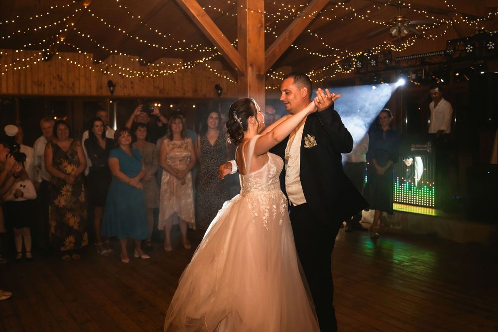 Wedding reception dance under romantic string lights with guests watching in background.