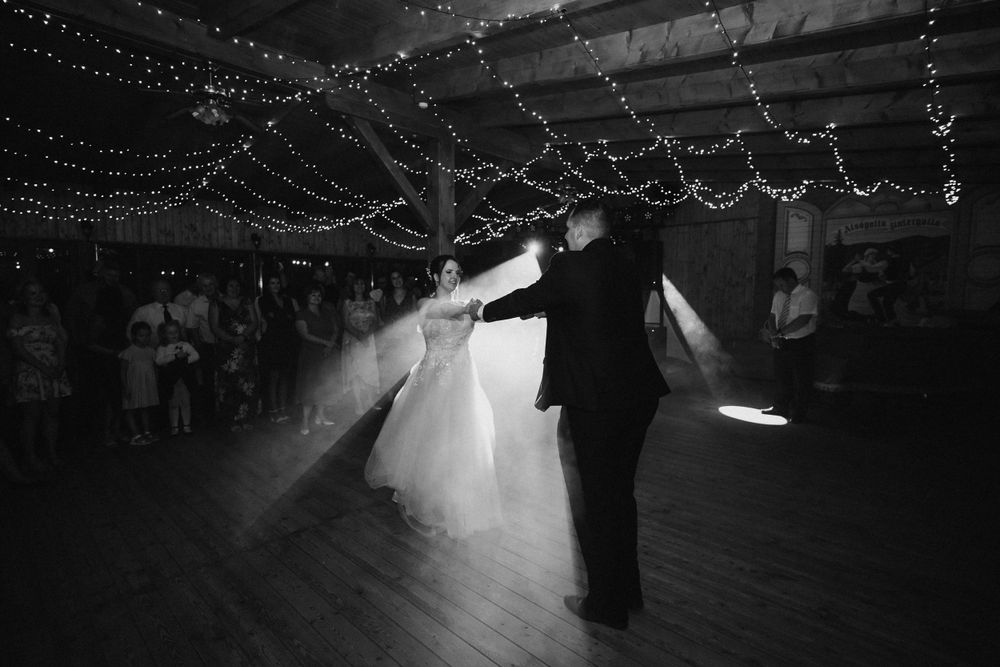 Black and white photo of dancing silhouettes under dreamy string lights in reception venue.