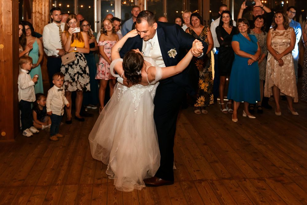 Romantic dip during wedding dance performance on wooden floor with guests watching.