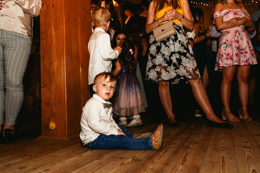Young child in formal wear sits on dance floor watching wedding celebration.