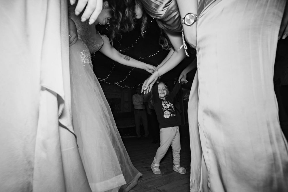 A black and white photo of guests dancing at a wedding reception on a dark dance floor.