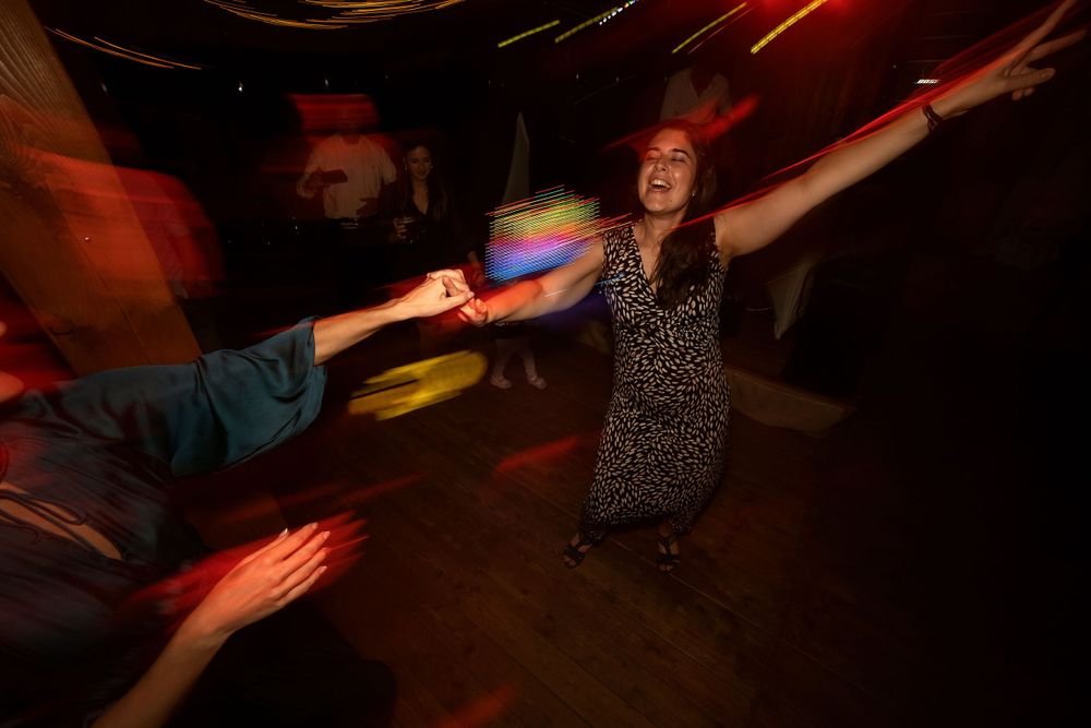 A person in a polka dot dress dancing energetically under red lighting at a party.