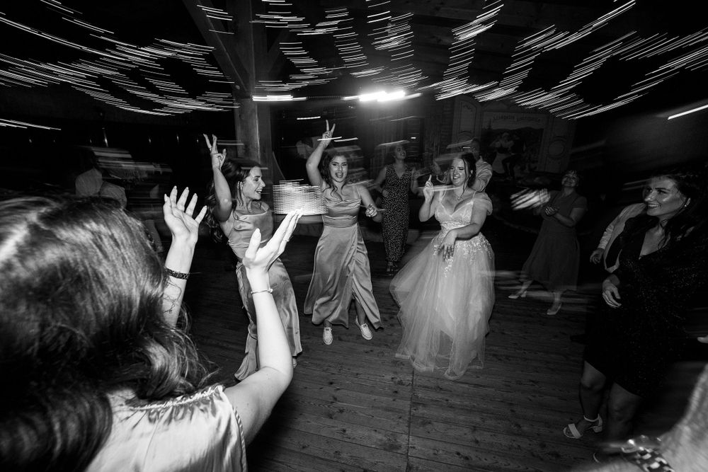 Wedding guests dancing with raised arms on a dark dance floor in black and white.