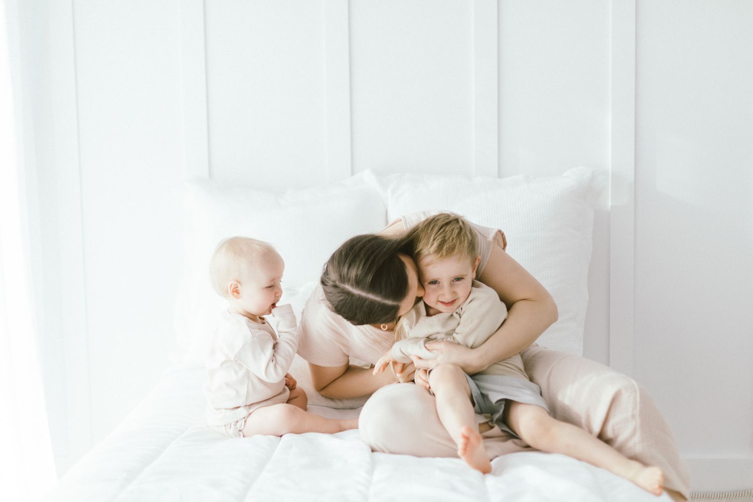 Sweet family cuddles together on white bedding.