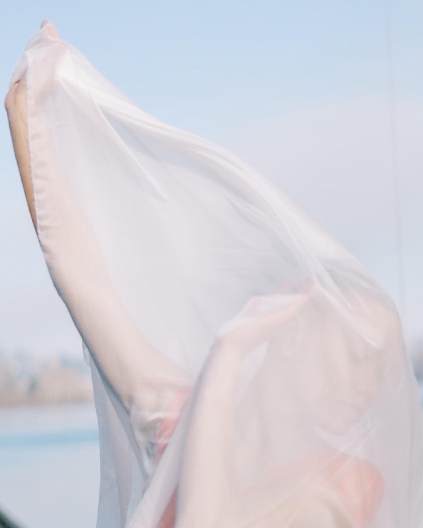 Flowing white fabric billowing against pale blue sky background.