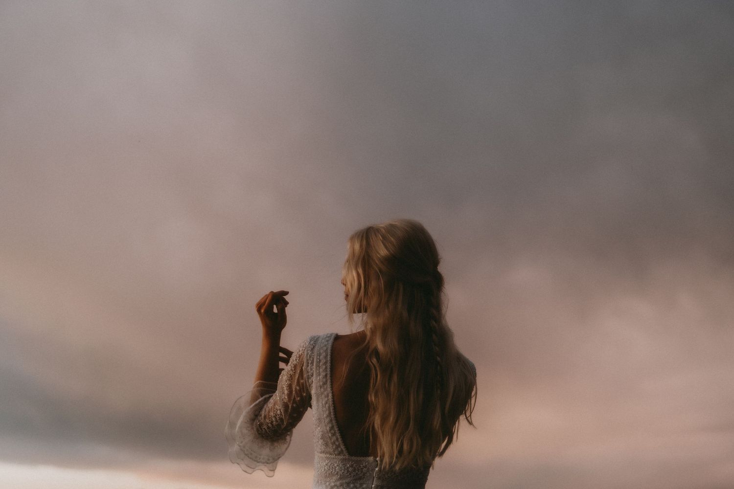 Dreamy silhouette of a woman in white dress against moody sunset sky with flowing hair.