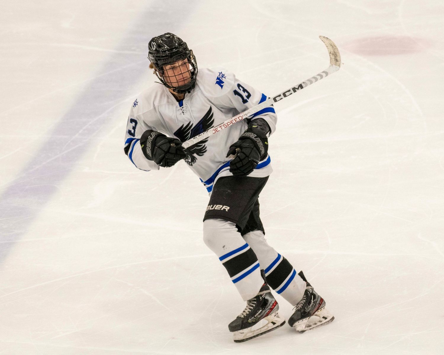 Hockey player in white jersey skating on ice with stick in motion.
