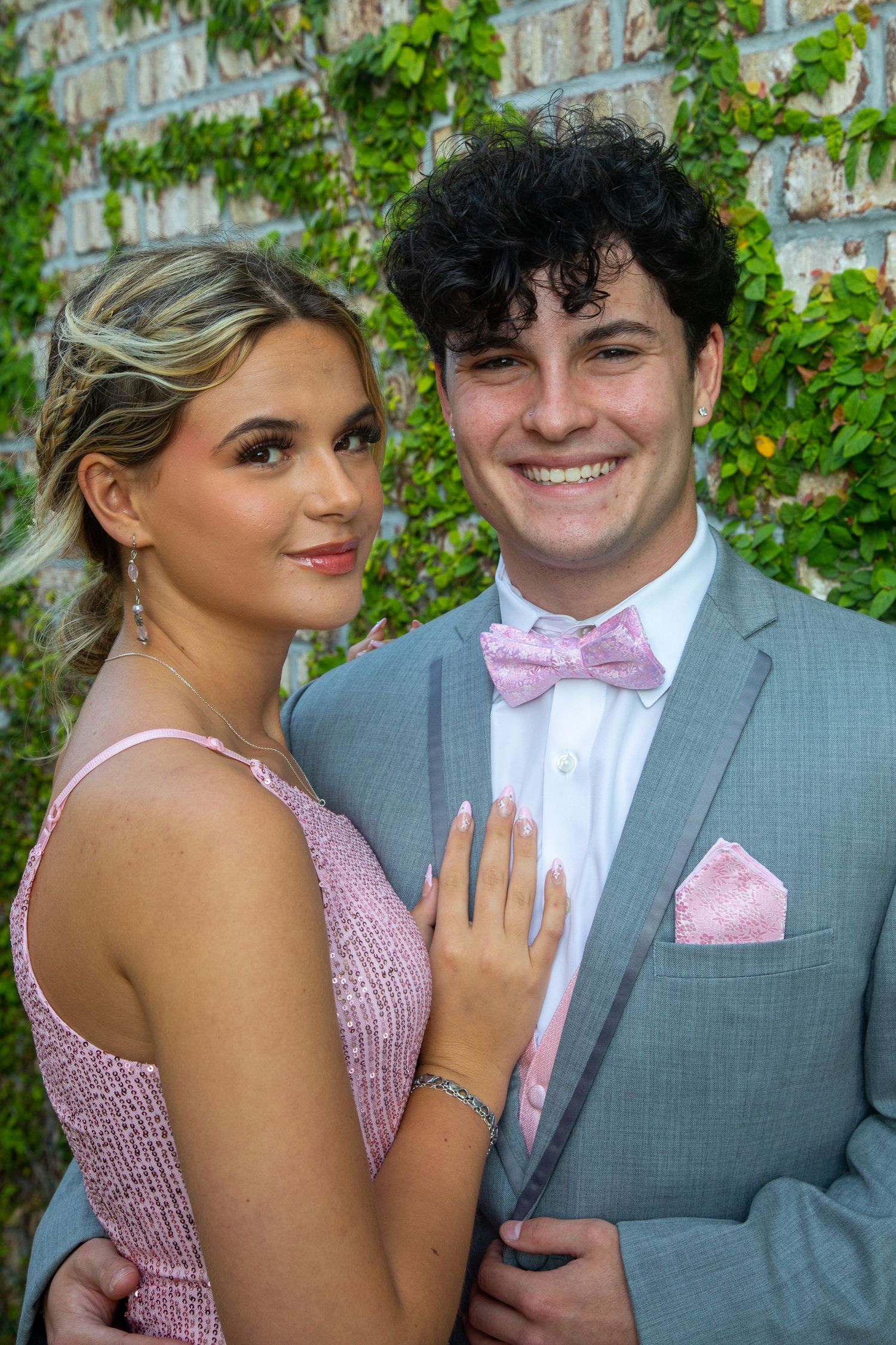 A dressed-up couple posing together for a formal portrait against an ivy-covered wall.