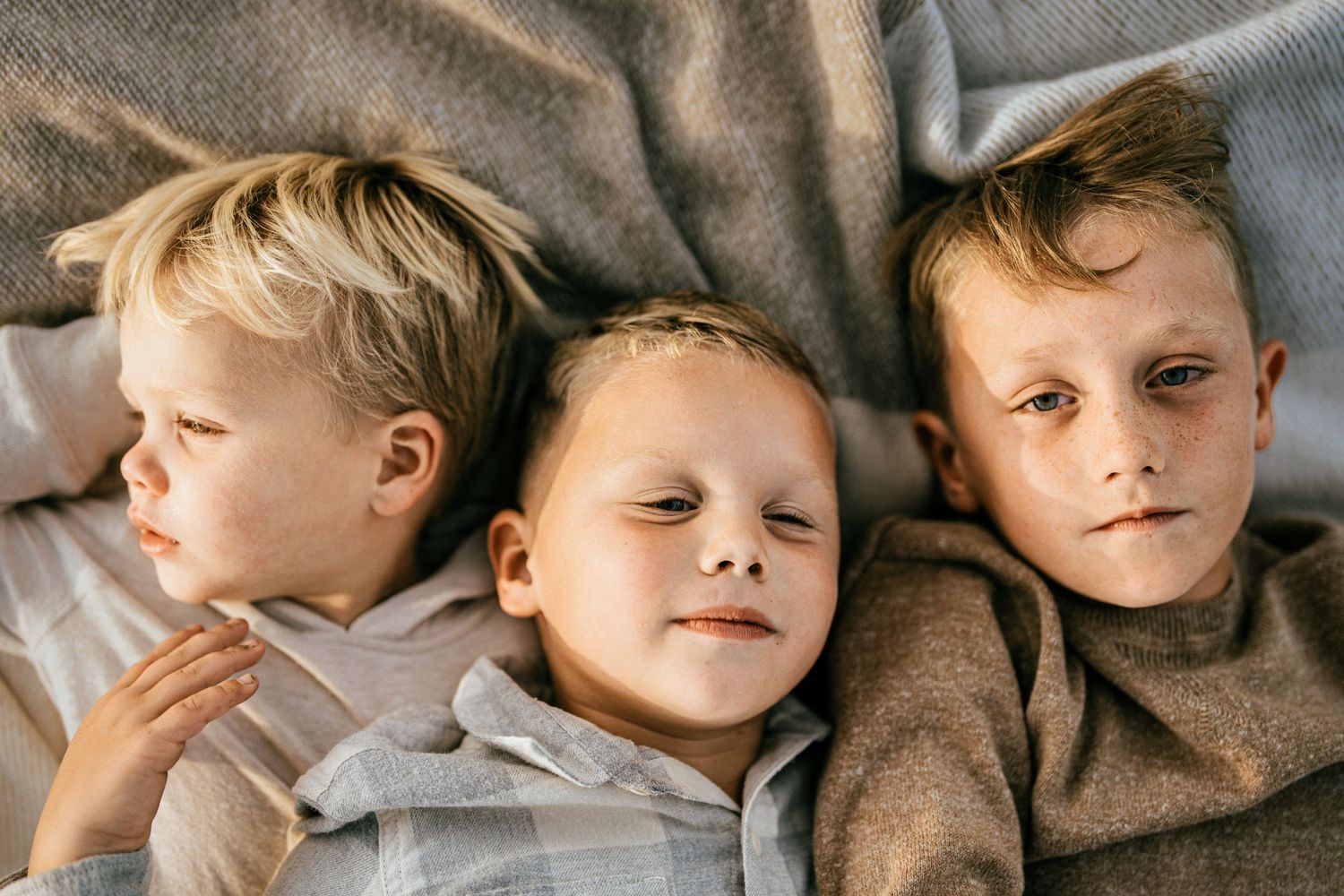 Three young boys lying on gray blanket with thoughtful expressions. sf bayarea family photographer , los gatos family photographer