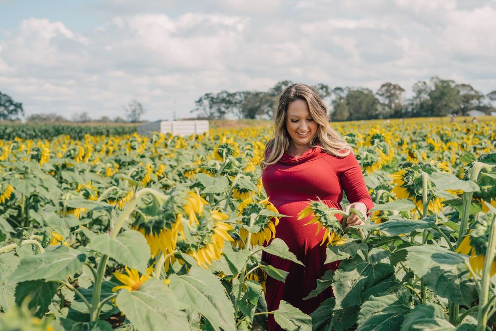 Woman in red dress poses in field of bright yellow sunflowers.