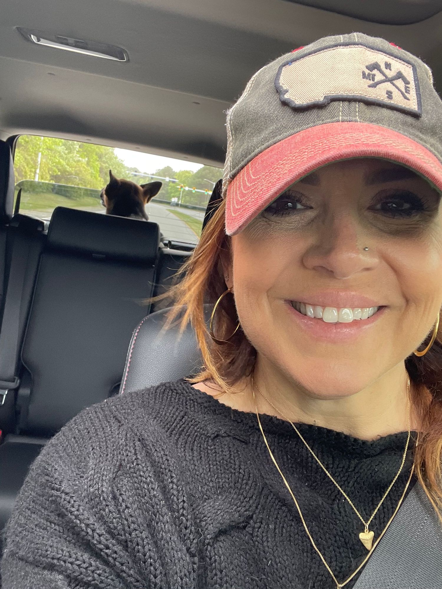 Car selfie showing a baseball cap and black sweater with a glimpse of the back seat.