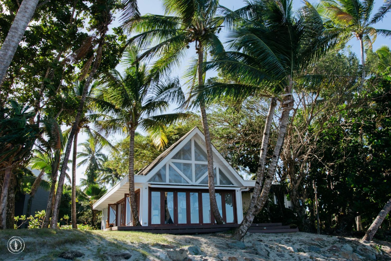 A white chapel with large windows nestled among tropical palm trees.