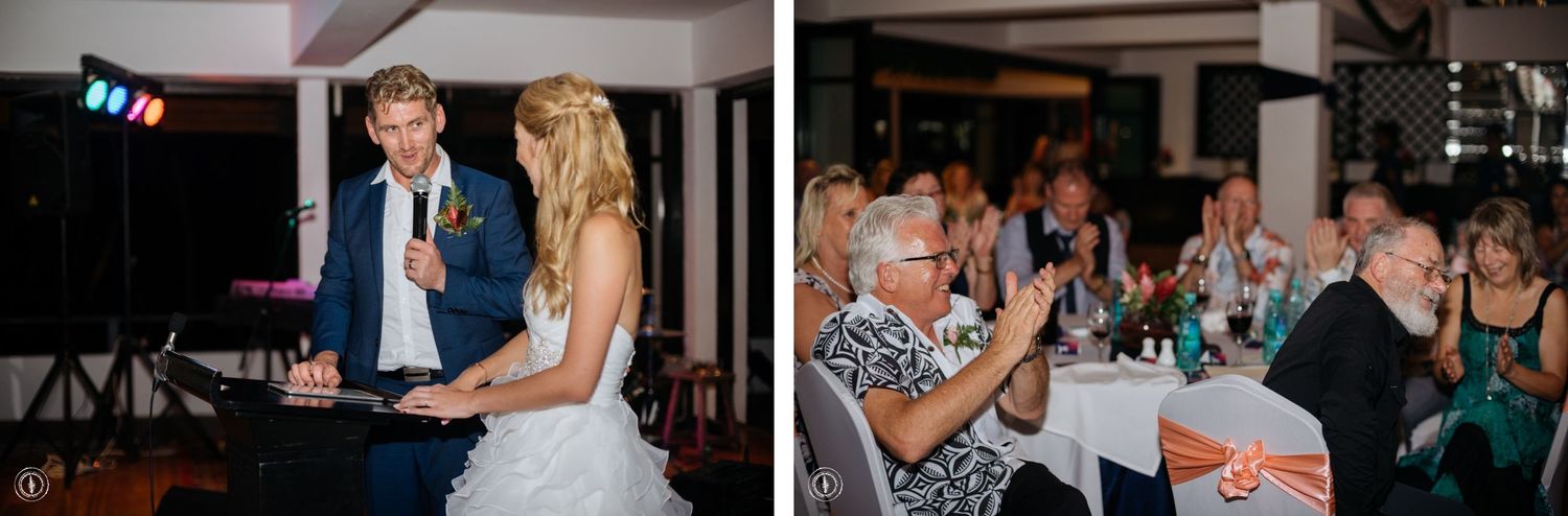 Couple sharing intimate moments during reception speeches with guests looking on.